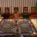 A colorful and ornate indoor religious altar with deity images, floral decorations, and lit lamps.